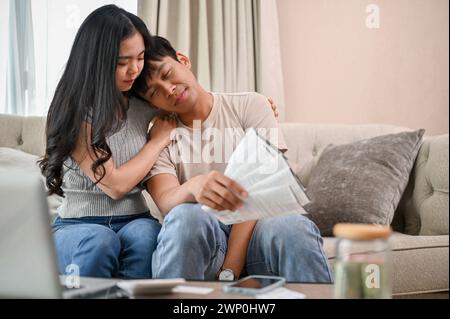 Eine fürsorgliche junge asiatische Frau unterstützt und ermutigt ihren gestressten Ehepartner auf dem Sofa. Das junge asiatische Paar macht sich Sorgen um die Haushaltsaussichten Stockfoto
