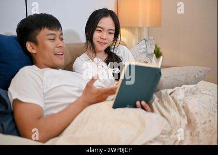 Ein glückliches junges asiatisches Paar im Pyjama liest gerne ein Buch zusammen, bevor es ins Bett geht. Paare und Hausleben Konzept Stockfoto