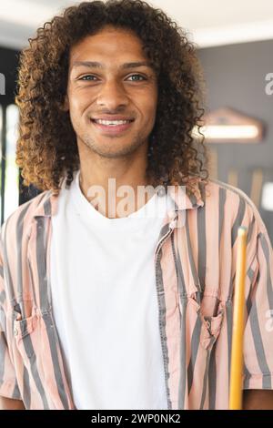 Ein junger birassischer Mann mit lockigen Haaren lächelt warm und hält einen Pool-Queue Stockfoto