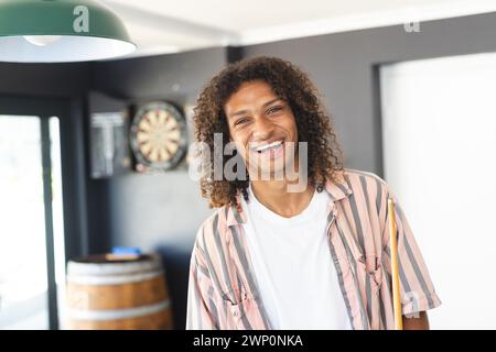 Ein junger birassischer Mann mit lockigen Haaren lächelt warm und trägt ein gestreiftes Hemd Stockfoto