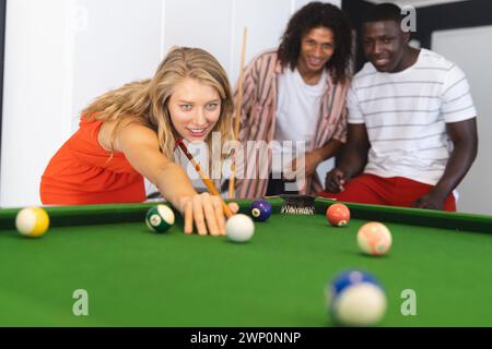 Junge kaukasische Frau spielt Billard, flankiert von einem rassistischen Mann und einem afroamerikanischen Mann Stockfoto