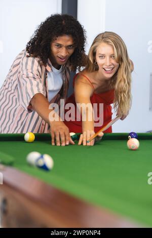 Ein birassischer Mann bringt einer kaukasischen Frau Billard bei, beide lächeln Stockfoto