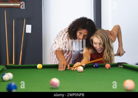 Ein birassischer Mann bringt einer kaukasischen Frau Billard bei, beide lächeln Stockfoto