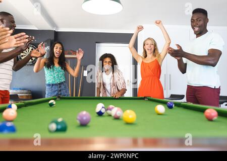 Verschiedene Freunde feiern an einem Billardtisch mit einem jungen Afroamerikaner, der klatscht Stockfoto