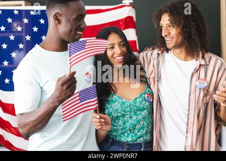 Ein afroamerikanischer Mann und ein birassisches Paar halten amerikanische Fahnen, alle tragen Sticker, die ich gewählt habe Stockfoto