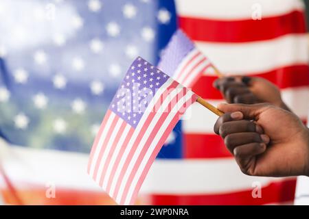 Afroamerikanische Hand mit einer kleinen amerikanischen Flagge, mit einer größeren Flagge im Hintergrund Stockfoto