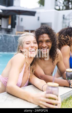 Junge kaukasische Frau und junger birassischer Mann lächeln am Pool und teilen einen freudigen Moment Stockfoto