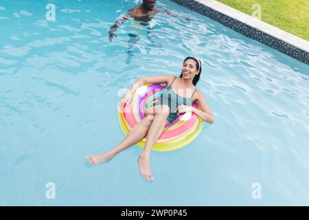 Eine junge Frau, die sich auf einem farbenfrohen Schwimmbecken aufhält, lächelt Stockfoto