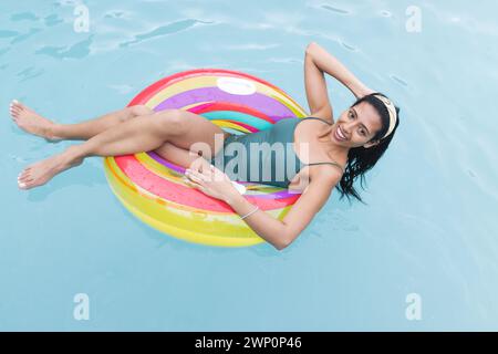 Die junge birassische Frau liegt auf einem farbenfrohen Schwimmbecken, ihr dunkles Haar ist zurückgebunden Stockfoto