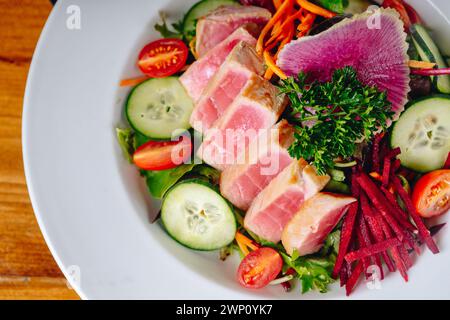 Ein Teller mit einer Vielzahl von Gemüse und Fleisch. Zu den Gemüsesorten gehören Gurken, Karotten und Tomaten. Das Fleisch wird in kleine Stücke geschnitten und Stockfoto