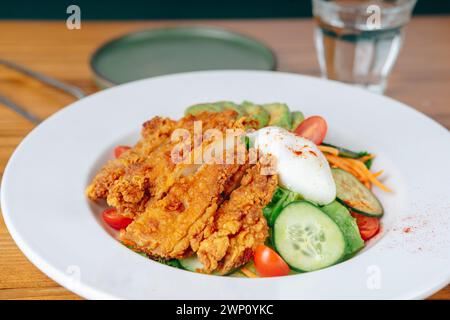 Ein Teller mit gebratenem Hähnchensalat mit einem Glas Wasser. Der Salat ist bunt und appetitlich, mit einer Vielzahl von Gemüse und einer großzügigen Menge an Chic Stockfoto