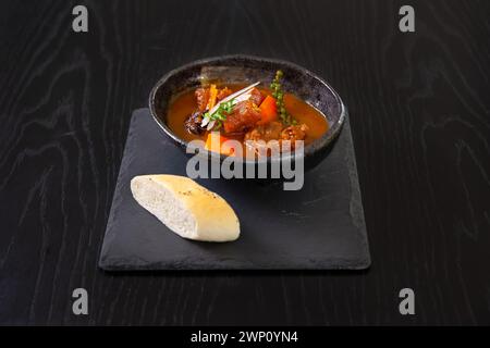 Rindfleisch gedünstet mit Kartoffeln, Karotten und Gewürzen isoliert auf schwarzem Holztischhintergrund Stockfoto