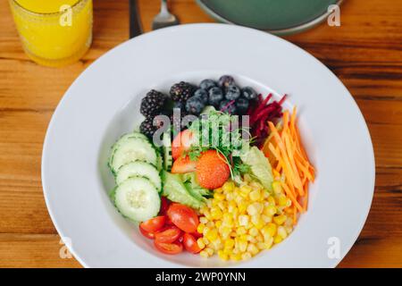 Ein farbenfroher Salat mit einer Vielzahl von Gemüse und Früchten, einschließlich Tomaten, Mais, Karotten und Beeren Stockfoto