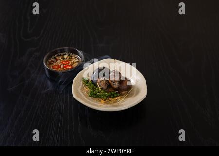 Mit Schweinefleisch gefüllte Schnecken, serviert auf weißem Teller, isoliert auf schwarzem Holztischhintergrund Stockfoto