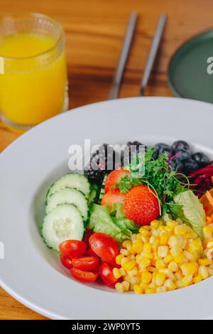 Ein bunter Salat mit einem Glas Orangensaft auf der Seite. Der Salat ist voller Gemüse und Obst, einschließlich Tomaten, Mais und Erdbeeren Stockfoto