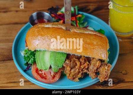 Ein Sandwich mit Avocado und Tomate auf einem blauen Teller. Ein Messer steht aus dem Sandwich Stockfoto