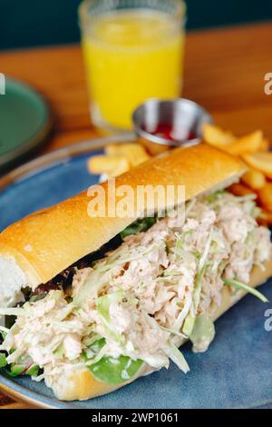 Ein Sandwich mit Salat und Fleisch auf einem blauen Teller. Ein Glas Orangensaft liegt auf dem Tisch Stockfoto