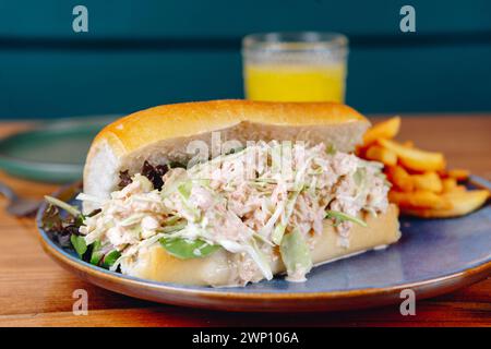 Ein Sandwich mit Salat und Huhn liegt auf einem Teller neben einem Glas Orangensaft. Das Sandwich wird in zwei Hälften geschnitten und auf eine blaue Platte gelegt Stockfoto