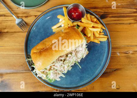 Ein Sandwich und Pommes sind auf einem blauen Teller. Das Sandwich wird in zwei Hälften geschnitten und hat eine Seite von Pommes Frites Stockfoto