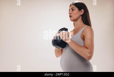 Schwangere Frauen trainieren in einem Studio, heben Gewichte und konzentrieren sich auf ihr Wohlbefinden während ihres dritten Trimenons. Sie legt Wert auf ihre Fitness und Selbstbestimmung Stockfoto