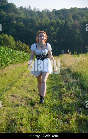 Eine hübsche junge Frau, die ein weißes, kurzes Kleid trägt, in grüner Natur vorwärts rennt Stockfoto