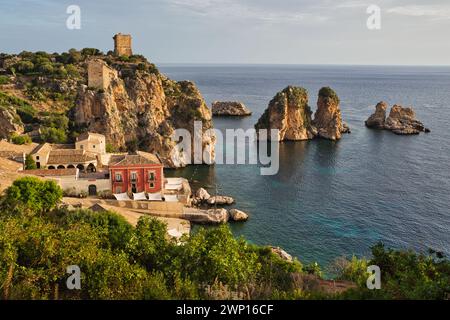 Tonnara di Scopello, Sizilien, früh am Morgen mit den faraglioni, Felsentürmen, im Meer und Verteidigungsturm auf dem Hügel Stockfoto