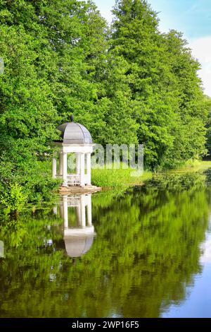 Weißer hölzerner Pavillon am Fluss, umgeben von Bäumen. Blick an einem ruhigen Sommermorgen mit klarem Himmel und Reflexionen auf dem Wasser. Stockfoto