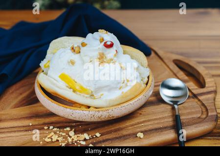 Eine Schüssel Eiscreme mit Nüssen darauf steht auf einem hölzernen Schneidebrett. Ein Löffel ist neben der Schüssel Stockfoto