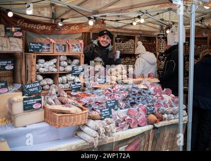 Lanslevillard, Frankreich, 10. Januar 2024: Ein guter Laune-Verkäufer, der hinter einem Stand mit lokalen Spezialitäten auf dem Marktplatz der Stadt steht Stockfoto