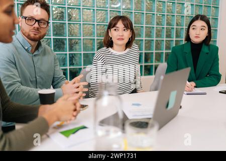 Nahaufnahme des multinationalen Startup-Teams, das gemeinsam am Meeting-Tisch Marketingberichte auf Papier diskutiert und Projektstatistiken erarbeitet Stockfoto