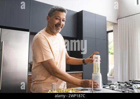 Biracial Senior man bereitet einen Smoothie in einer modernen Küche zu Stockfoto
