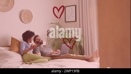 Bild von Herzen über verschiedenartiges Paar mit Laptop im Bett Stockfoto