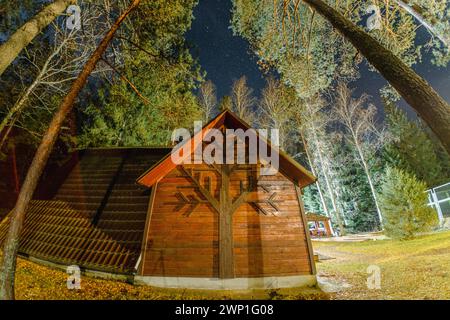 Malerisches kleines Holzhaus eingebettet in eine natürliche Landschaft mit einem Baum an der Seite, umgeben von Kiefern unter Sternenhimmeln Stockfoto