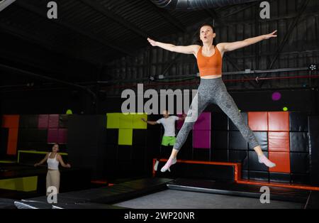 Glückliche Frau mittleren Alters, die auf Trampolinen in einem Sporthalle trampoliniert und springt, Workout und modernes Unterhaltungskonzept Stockfoto