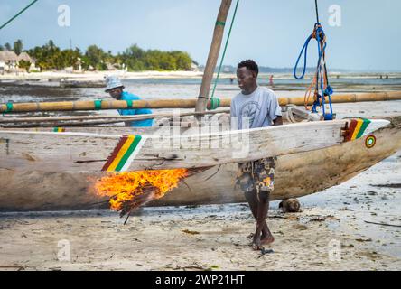 Fischer verwenden brennende Palmwedel, um sein traditionelles hölzernes Dhow-Boot Jambiani, Sansibar, Tansania zu sairieren und zu wasserdicht zu machen Stockfoto