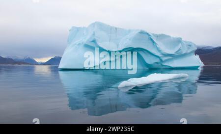 Großer, blau gefärbter Eisberg mit Knittermuster schwimmt vor Nanortalik in Grönland mit Reflexion in ruhigem, noch arktischem Meereswasser Stockfoto