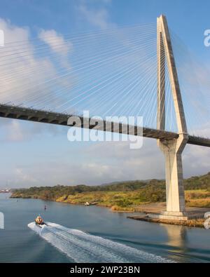 Ein kleines Boot passierte unter der großen beeindruckenden Atlantikbrücke bei Colon Panama am Anfang des Panamakanals, der sich vor dem blauen Himmel mit niedrigen Wasserständen befindet Stockfoto