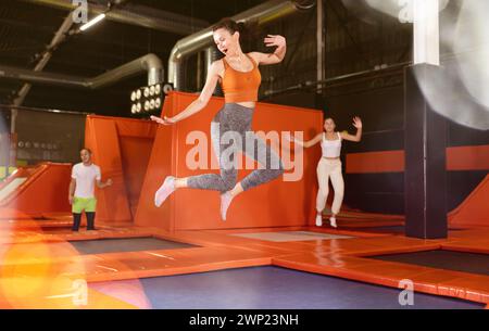 Glückliche Frau mittleren Alters, die auf Trampolinen in einem Sporthalle trampoliniert und springt, Workout und modernes Unterhaltungskonzept Stockfoto
