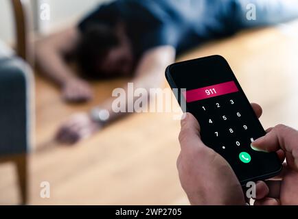 Notruf 911. Unfall oder Epilepsie. Bewusstloser, ohnmächtiger junger Mann, der auf dem Boden liegt. SOS-Ambulanzalarm mit Telefon in der Hand. Stockfoto