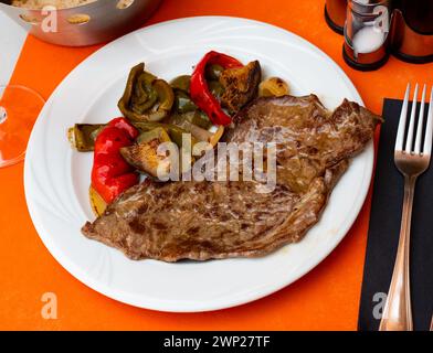 Auf dem runden weißen Teller liegt eine saftige gebratene Scheibe Rinderfilet, garniert mit gedünstetem Gemüse. Stockfoto