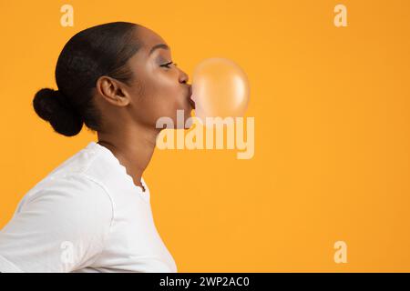 Profilaufnahme einer afroamerikanischen Dame, die Bubblegum bläst, orange Hintergrund Stockfoto