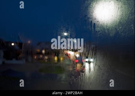 Farbige, winterliche, regnerische Nachtsicht durch Busfenster, Straßenlaternen, Autoscheinwerfer, Straßenlaternen, Ampeln, nebliges Fenster und Regentropfen Stockfoto