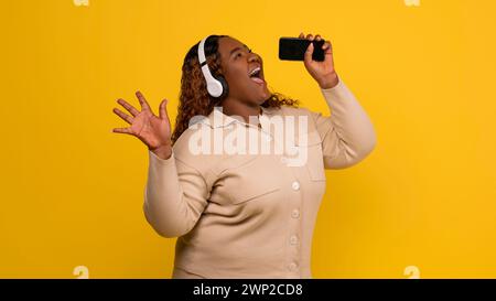 Süße, mollige afroamerikanerin, die Karaoke auf gelbem Hintergrund singt Stockfoto