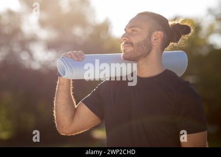 Sportlicher Kerl, bereit, im Park zu trainieren und Yoga-Matte zu halten Stockfoto