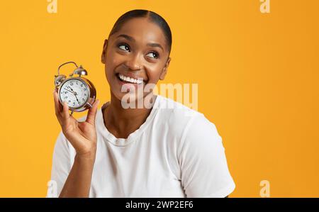 Fröhliche schwarze Millennial-Frau, die Wecker auf gelbem Hintergrund hält Stockfoto