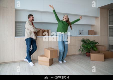 Die Frau hob die Hände hoch, erfreuen sich an einem neuen Zuhause. Der zufriedene Ehemann beobachtet das Glück der Frau mit Emotionen. Stockfoto