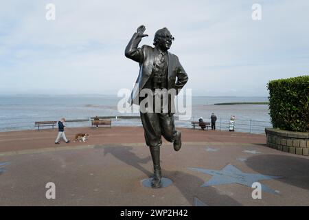 Eric Morecambe Statue mit Blick auf das Meer in Morecambe, Lancashire. Die 1999 von der Königin enthüllte Statue zeigt Eric Morecambe in einer seiner charakteristischen Posen mit einem Fernglas um den Hals (er war ein leidenschaftlicher Ornithologe). Die Statue steht vor der atemberaubenden Kulisse der Morecambe Bay und der Lake District Hügel Stockfoto