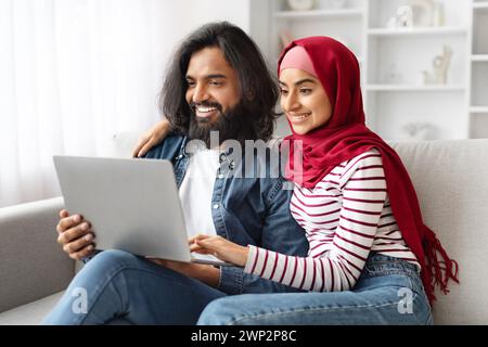 Porträt Glücklicher Muslimischer Ehegatten, Die Sich Zu Hause Mit Einem Laptop Entspannen Stockfoto