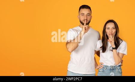 Leise selbstbewusste Mann und Frau in weißen Hemden, die Finger auf die Lippen legen, in einer „Shush“-Geste Stockfoto