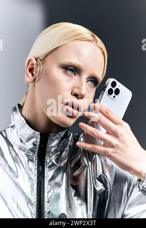 Ansprechende Frau in futuristischem Silber-Outfit posiert mit Telefon und blickt vor grauem Hintergrund weg Stockfoto